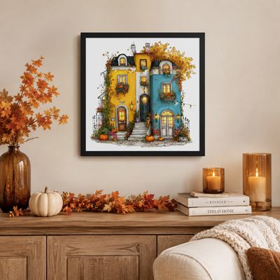 Black framed autumn house print above a wooden sideboard with fall leaves, white pumpkin, amber candles, and cozy decor.