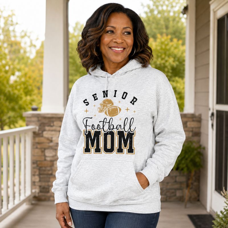 Black woman wearing ash Senior Football Mom hoodie with black and gold football design on a fall porch