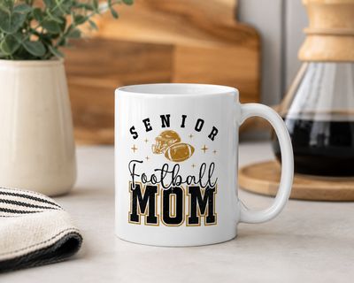 Senior Football Mom coffee mug with black and gold football graphics displayed on a kitchen counter.