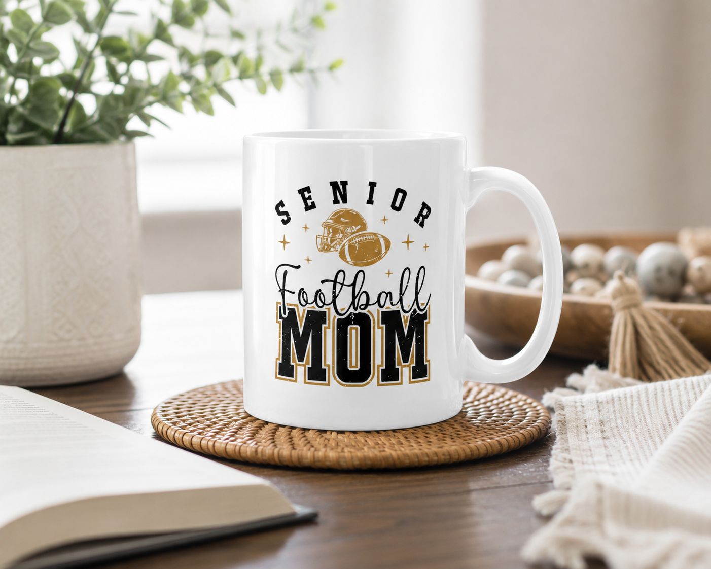Senior Football Mom ceramic mug with black and gold football design in a bright cozy home setting.