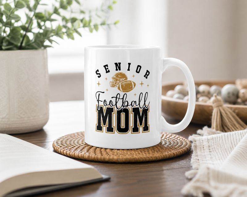 Senior Football Mom ceramic mug with black and gold football design in a bright cozy home setting.