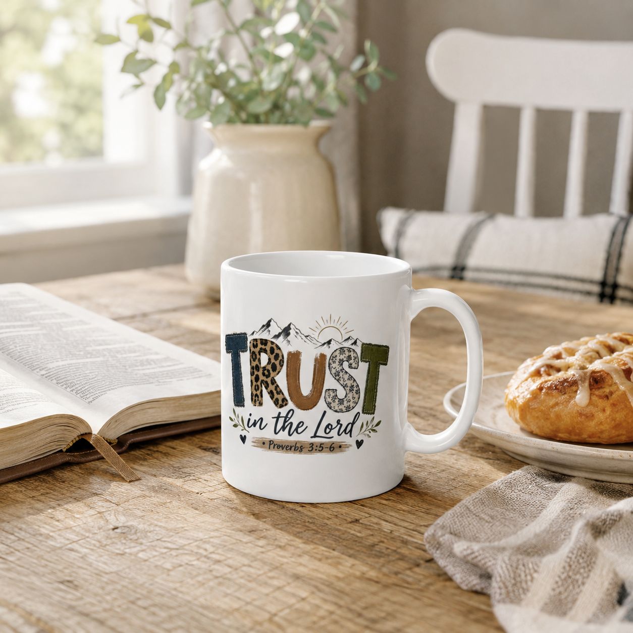 White Christian mug with “Trust in the Lord” Proverbs 3:5-6 design beside an open Bible and pastry on a rustic table.