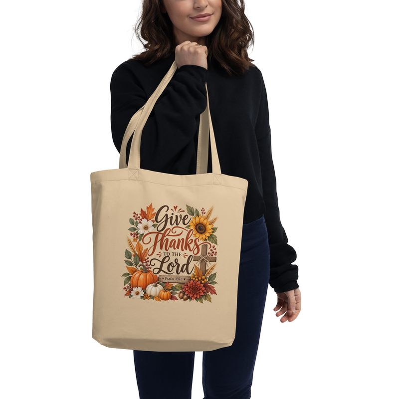 Woman carrying an Oyster Christian fall tote bag featuring Give Thanks to the Lord Psalm 107:1 with pumpkins and autumn flora