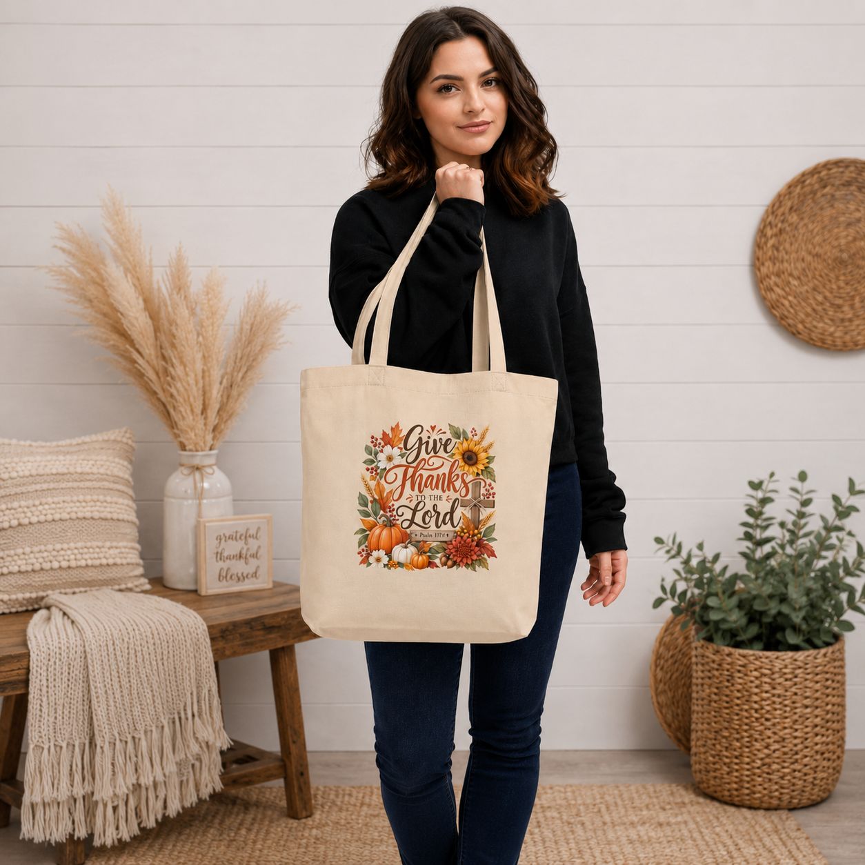 Square lifestyle mockup of woman carrying Psalm 107:1 Christian fall tote bag with pumpkins, sunflowers, and autumn leaves.