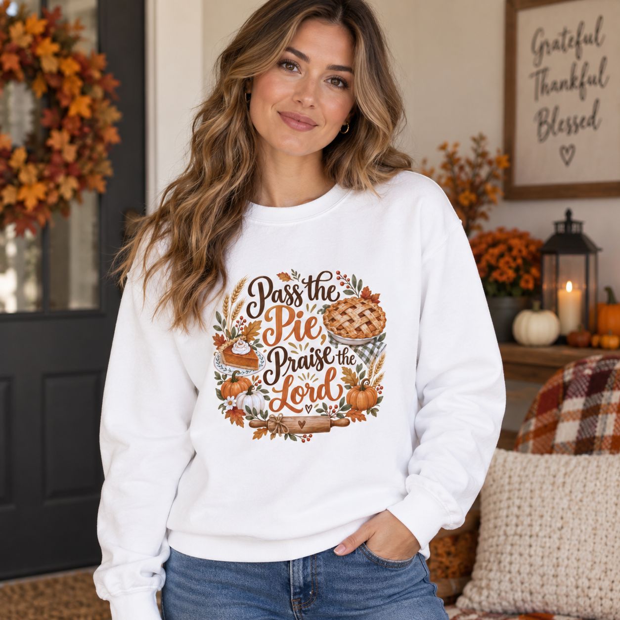 Woman wearing white Pass the Pie Praise the Lord Christian Thanksgiving sweatshirt in a warm fall home setting with pumpkins 