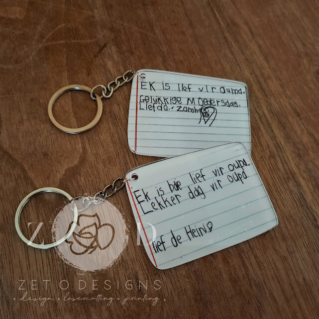 Close-up of a clear acrylic keyring featuring a custom-printed handwritten note in black ink.