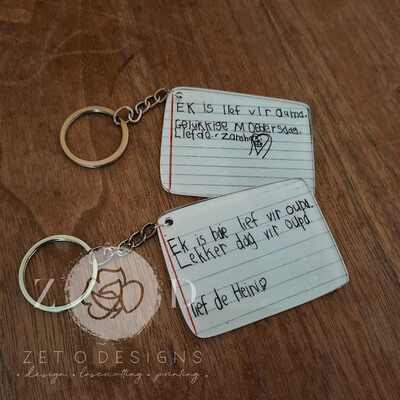 Close-up of a clear acrylic keyring featuring a custom-printed handwritten note in black ink.
