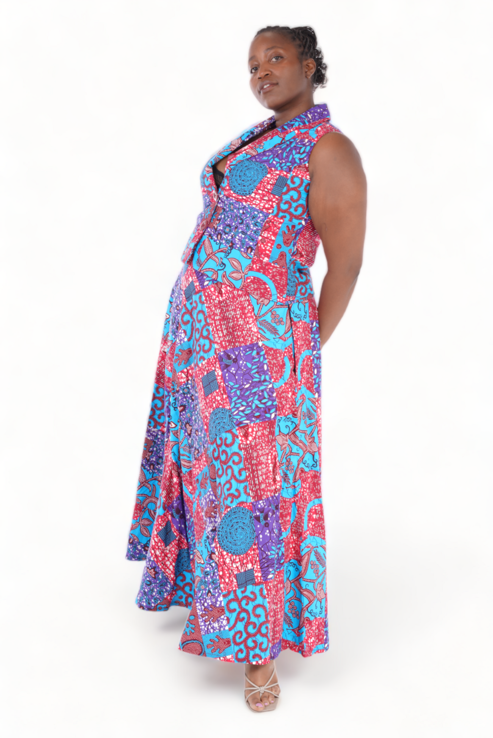 Woman posing in a vibrant, sleeveless patchwork dress featuring red, blue, and purple patterns, exuding confidence and elegance. White background.