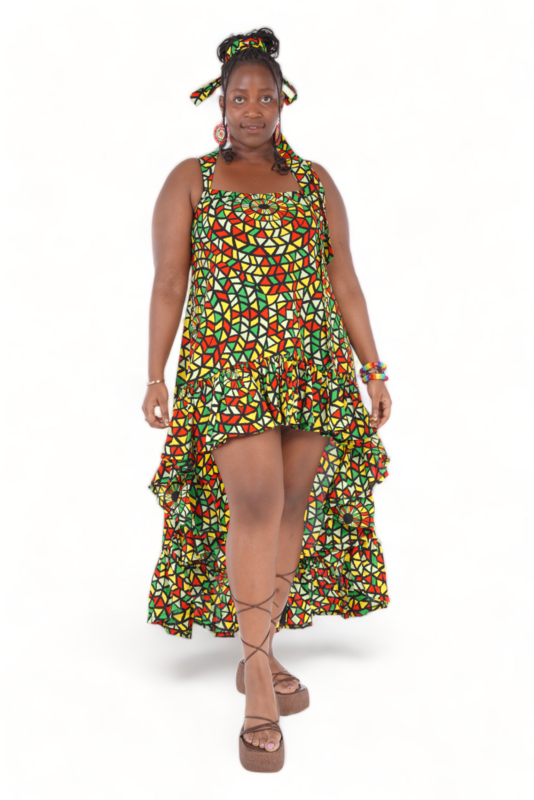 Woman wearing a vibrant, geometric-patterned high-low dress with red, yellow, and green colors. She accessorizes with a matching headband, earrings, and bracelets, showcasing a joyful, confident expression.