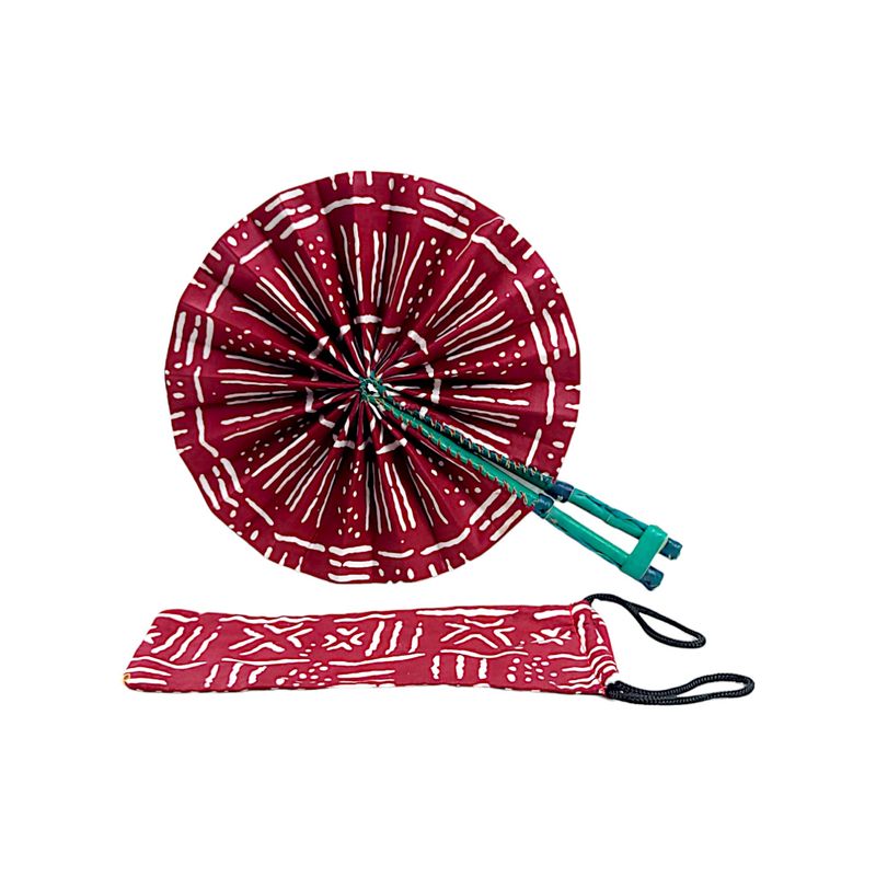 A vibrant, circular hand fan with red fabric decorated by white, symmetrical geometric patterns. The green handle is folded, adding a contrasting element.
