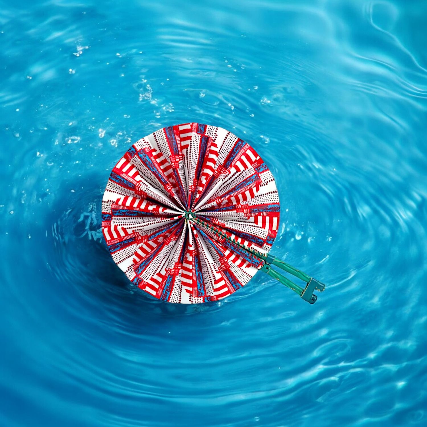 A vibrant circular hand fan with a pattern of red, white, and blue geometric shapes. It has a green handle, evoking a lively and festive tone.
