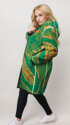 A person in black leggings and white sneakers poses confidently in a vibrant green coat with yellow and orange patterns, exuding a stylish, cozy vibe.