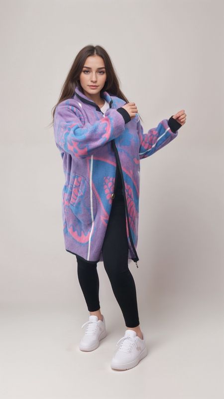 Young woman in a vibrant purple and blue patterned coat poses confidently. She wears black leggings and white sneakers, against a neutral backdrop.