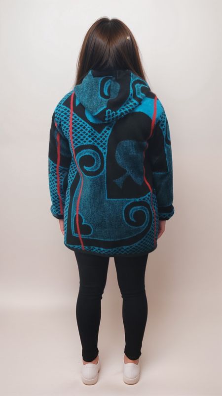A person from behind wearing a blue and black patterned hoodie with swirls and shapes, black leggings, and white shoes, standing against a plain backdrop.