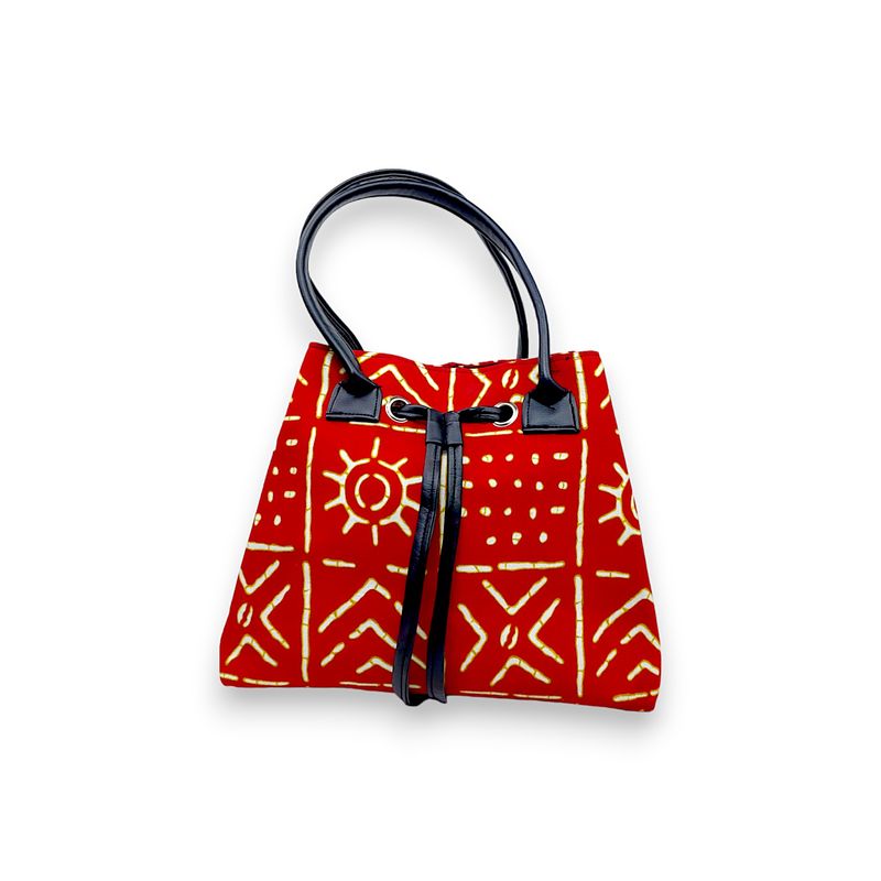 Red handbag with intricate yellow tribal patterns, black leather handles, and a drawstring closure. The design feels vibrant and artistic.