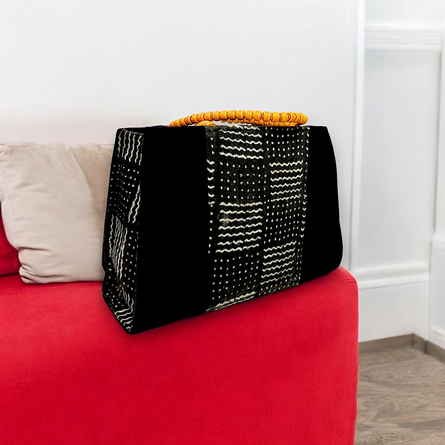 Black handbag with a woven, geometric white pattern. Features a bold orange beaded handle, creating a modern yet traditional aesthetic.