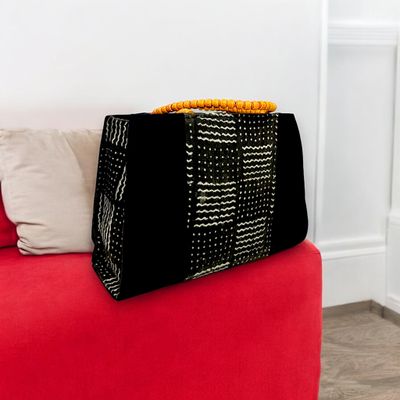 Black handbag with a woven, geometric white pattern. Features a bold orange beaded handle, creating a modern yet traditional aesthetic.