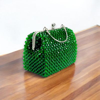 Elegant green beaded handbag with shimmering crystals and a silver clasp handle, set against a black background. The tone is luxurious and sophisticated.