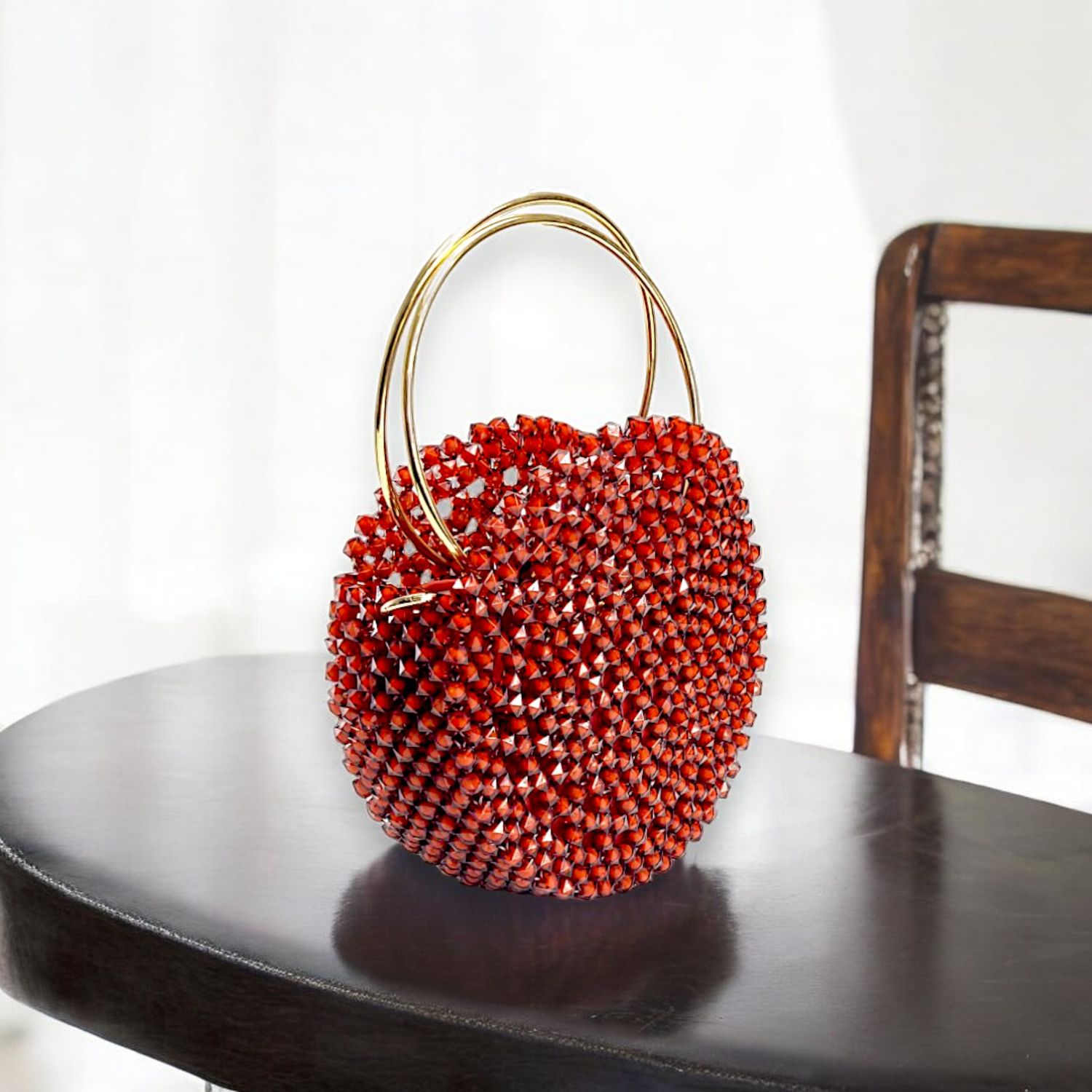 A striking round handbag adorned with small red crystals, featuring two elegant gold rings as handles, set against a black background, exuding luxury.
