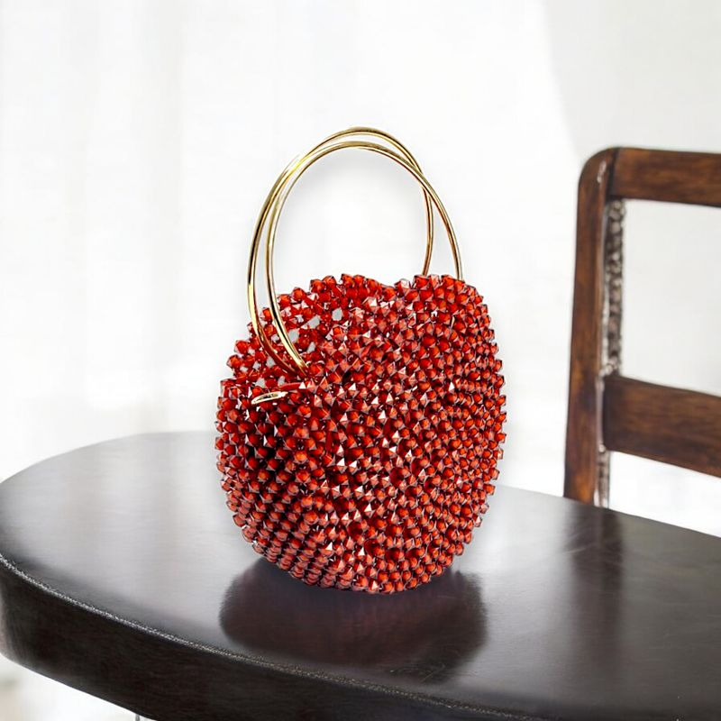 A striking round handbag adorned with small red crystals, featuring two elegant gold rings as handles, set against a black background, exuding luxury.