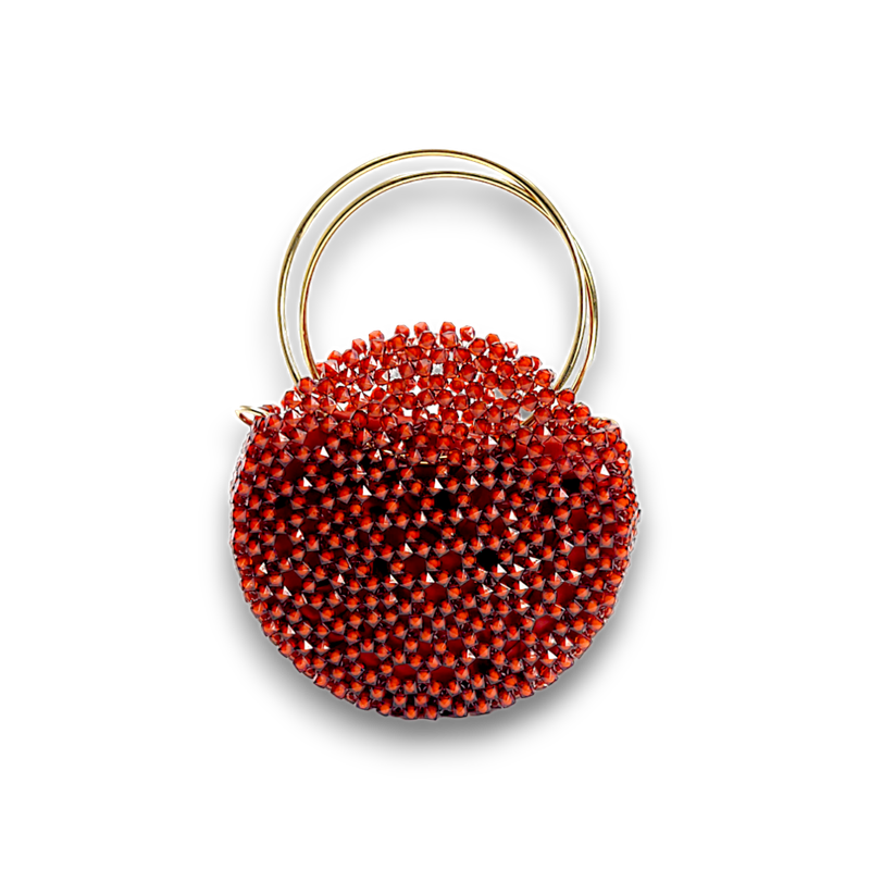 A striking round handbag adorned with small red crystals, featuring two elegant gold rings as handles, set against a black background, exuding luxury.