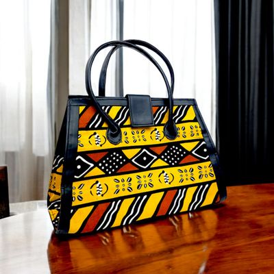 Colorful handbag with black leather handles and trim, featuring vibrant yellow, orange, and black geometric and floral patterns. Energetic and stylish.