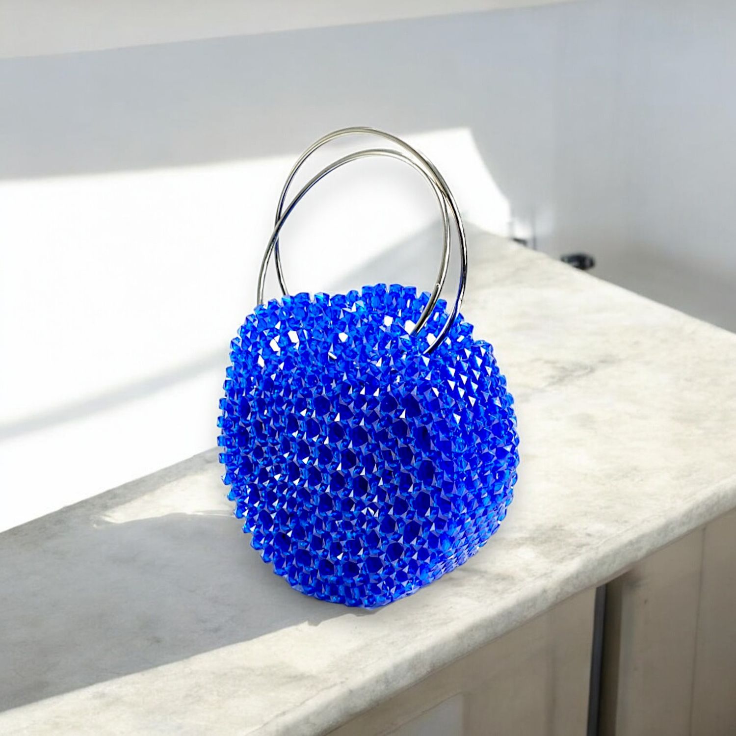 A vibrant blue spherical handbag adorned with sparkling crystals and a silver handle against a black background, conveying elegance and luxury.