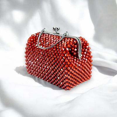 Elegant ruby beaded handbag with shimmering crystals and a silver clasp handle, set against a black background. The tone is luxurious and sophisticated.