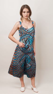 A woman in a vibrant, patterned dress with swirling blue and orange designs stands against a plain background, conveying a relaxed, confident mood.