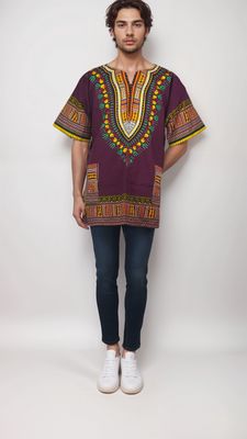 A man models a vibrant reddish and yellow African print shirt, showcasing a stylish burgundy daishiki design.