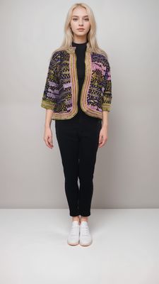 A woman stands confidently, wearing a colorful embroidered jacket over a black top and pants, with white sneakers. The tone is stylish and modern.