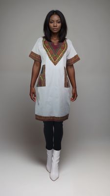 A woman models a white tunic featuring vibrant ethnic designs, showcasing a stylish African print daishiki shirt dress.