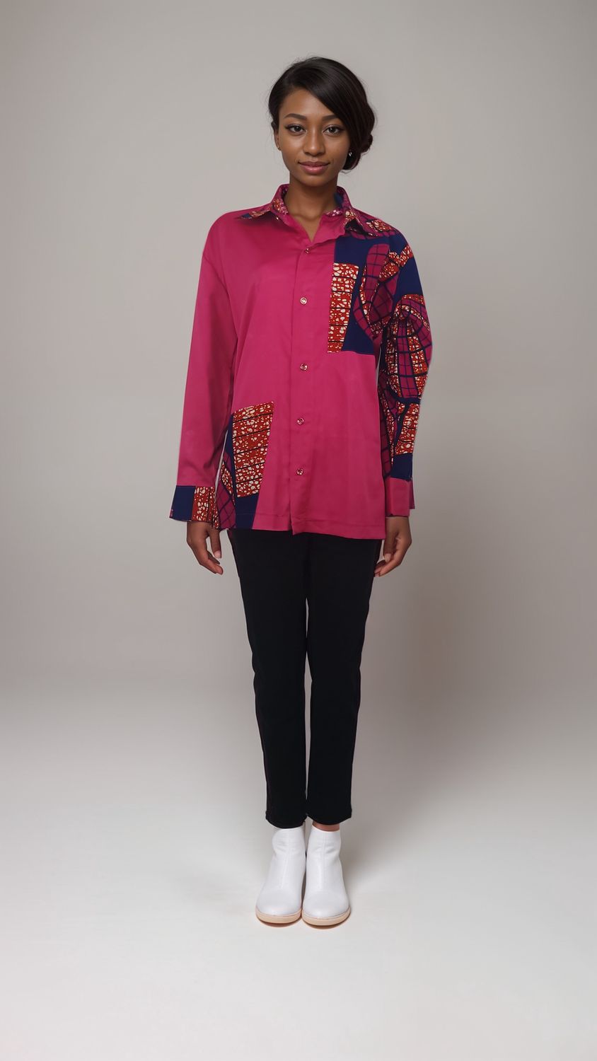 A woman wearing a pink African print shirt and jeans stands confidently, showcasing a vibrant and stylish outfit.