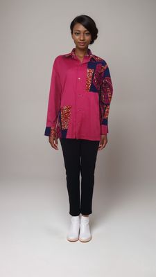 A woman wearing a pink African print shirt and jeans stands confidently, showcasing a vibrant and stylish outfit.