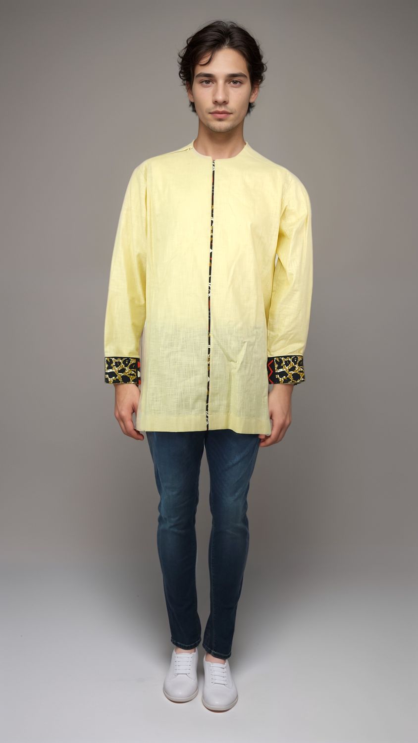 A man dressed in a vibrant yellow shirt and denim jeans poses casually, exuding a cheerful demeanor
