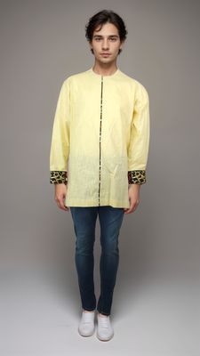 A man dressed in a vibrant yellow shirt and denim jeans poses casually, exuding a cheerful demeanor