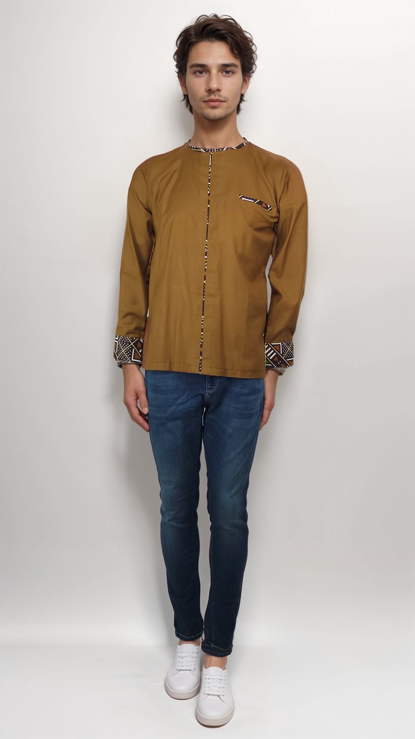 A man wearing a brown shirt and jeans stands confidently, showcasing a casual yet stylish look