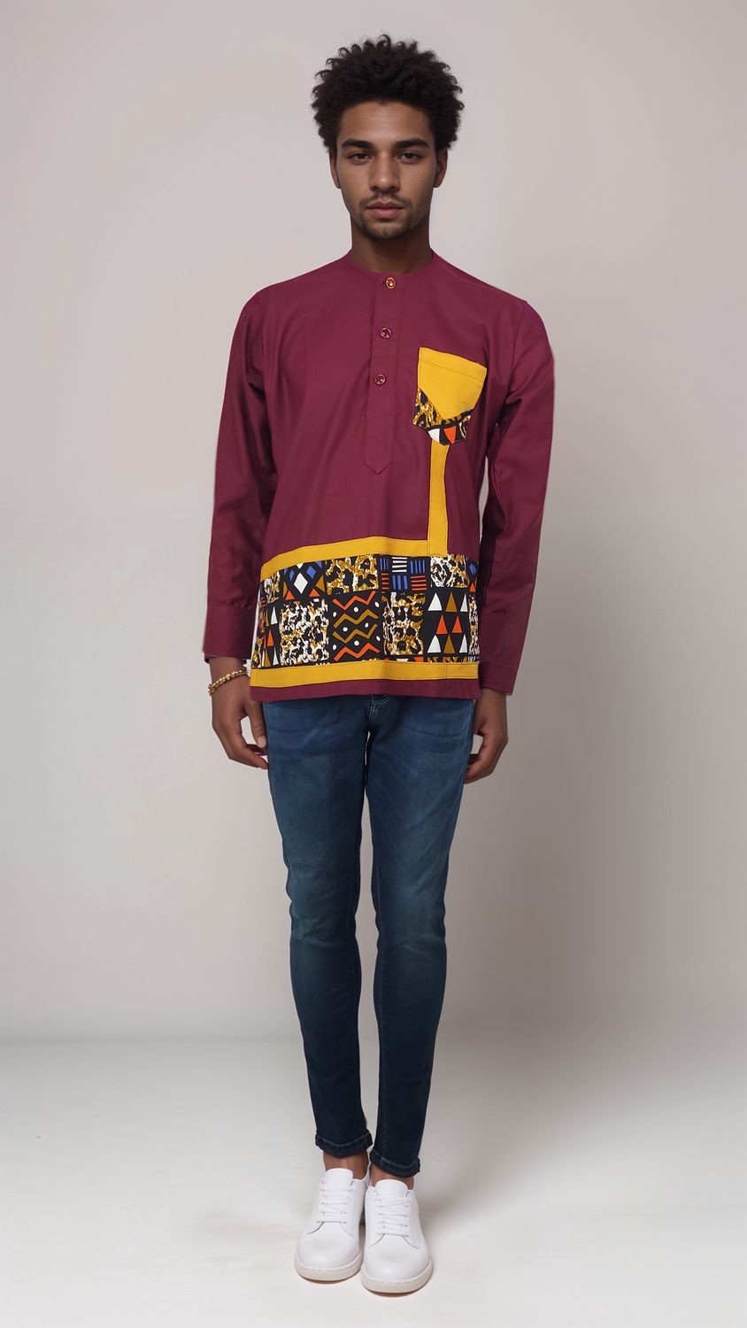 A man in a maroon shirt featuring vibrant African print patterns, standing confidently with a warm smile.