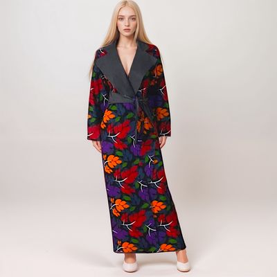 A woman with long blond hair wears a dark, floral-patterned dress with vibrant red, orange, and purple leaves, projecting a calm and elegant tone.
