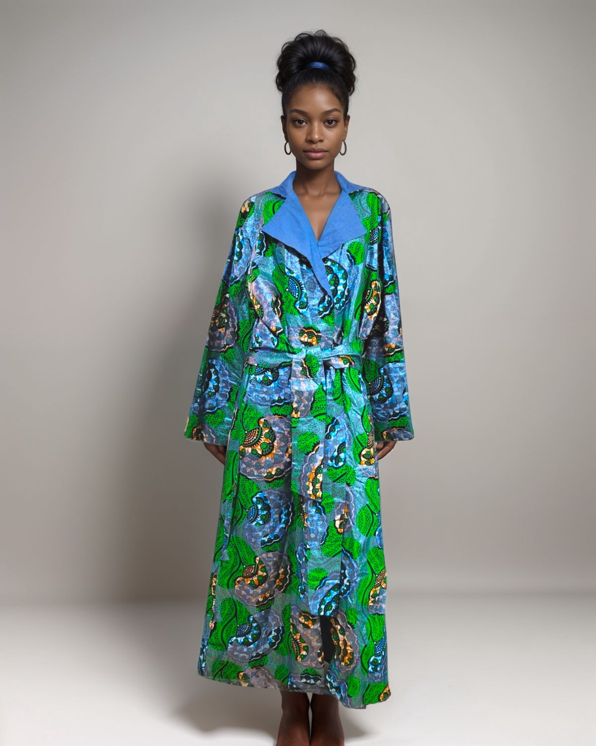 A woman gracefully wears a vibrant green and blue African print robe, showcasing her cultural heritage and style