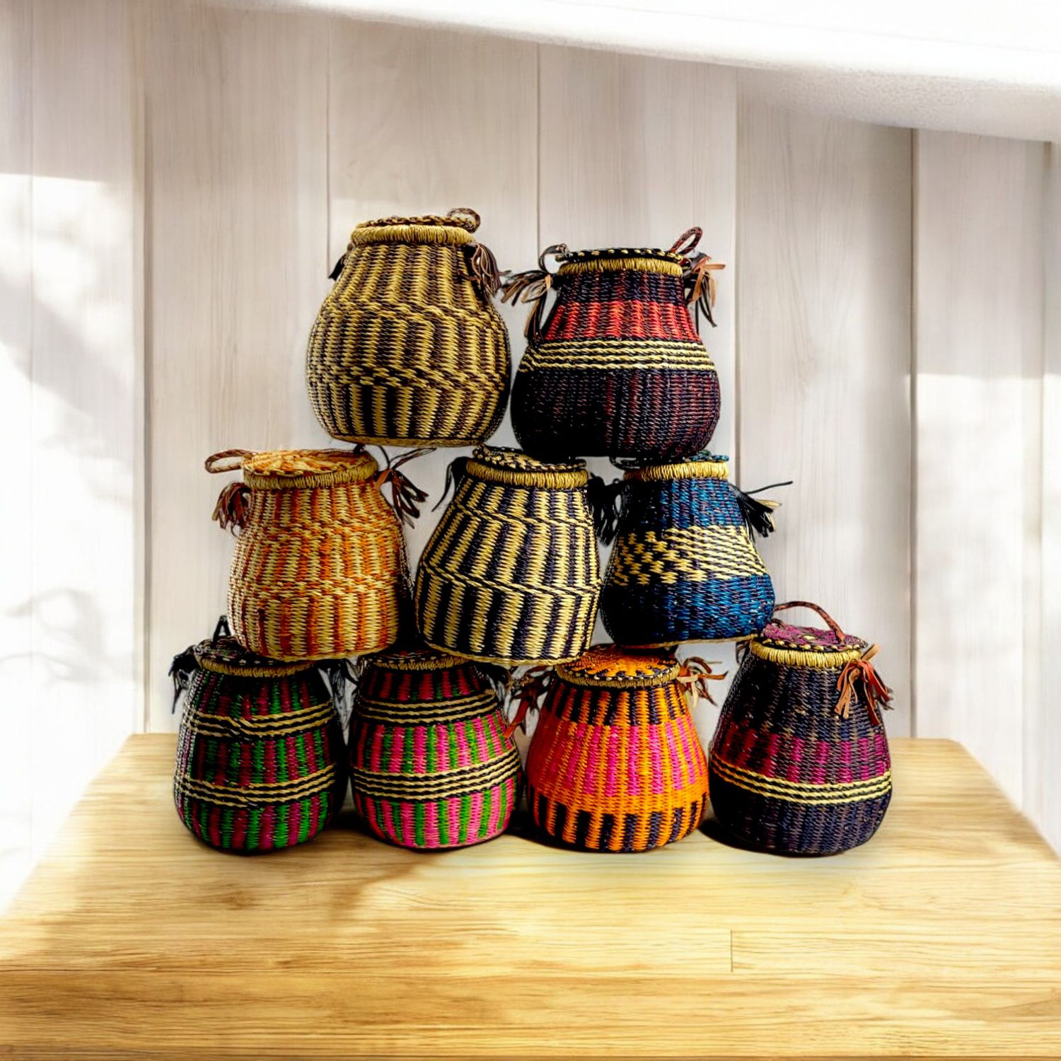 Nine colorful woven baskets are stacked in a pyramid. Each basket features intricate patterns in hues of brown, red, blue, yellow, and orange on a wooden surface.