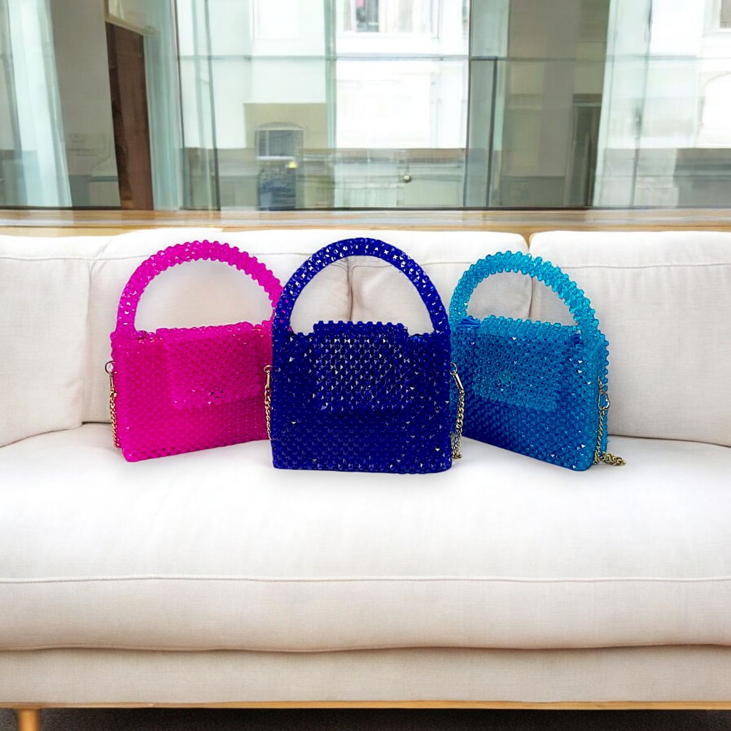 Three colorful, beaded handbags in pink, blue, and teal are artfully displayed on a concrete pedestal against a minimalist white background.