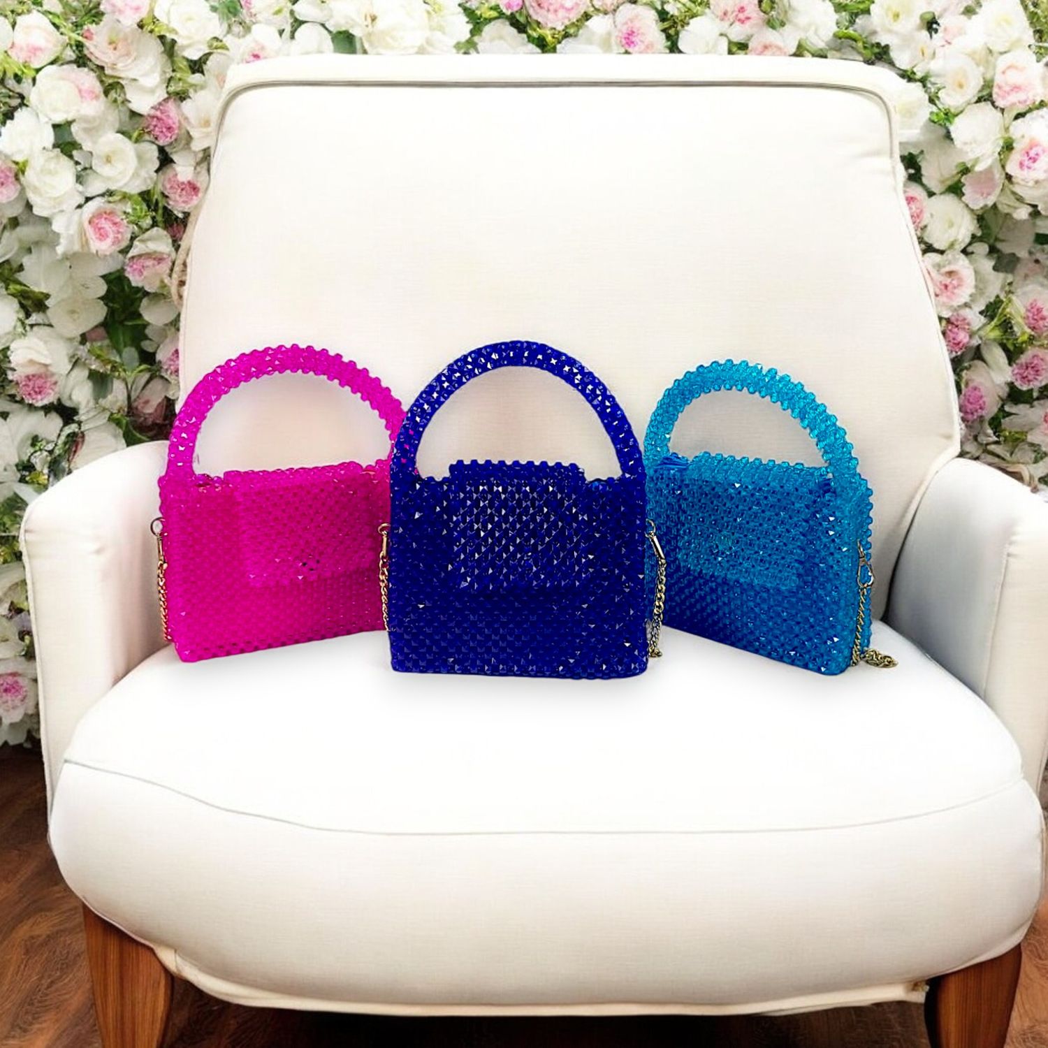 Three colorful, beaded handbags in pink, blue, and teal are artfully displayed on a concrete pedestal against a minimalist white background.