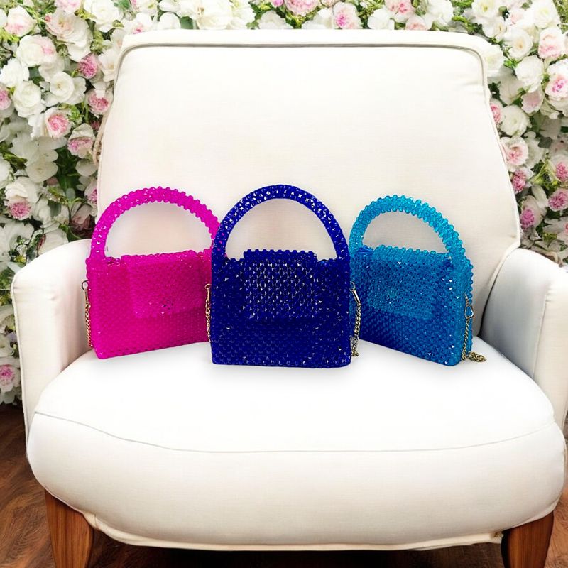 Three colorful, beaded handbags in pink, blue, and teal are artfully displayed on a concrete pedestal against a minimalist white background.