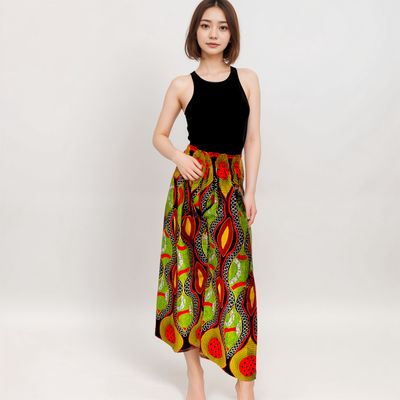 A woman in a black sleeveless top and a vibrant, colorful skirt with geometric patterns stands against a white background, exuding confidence.