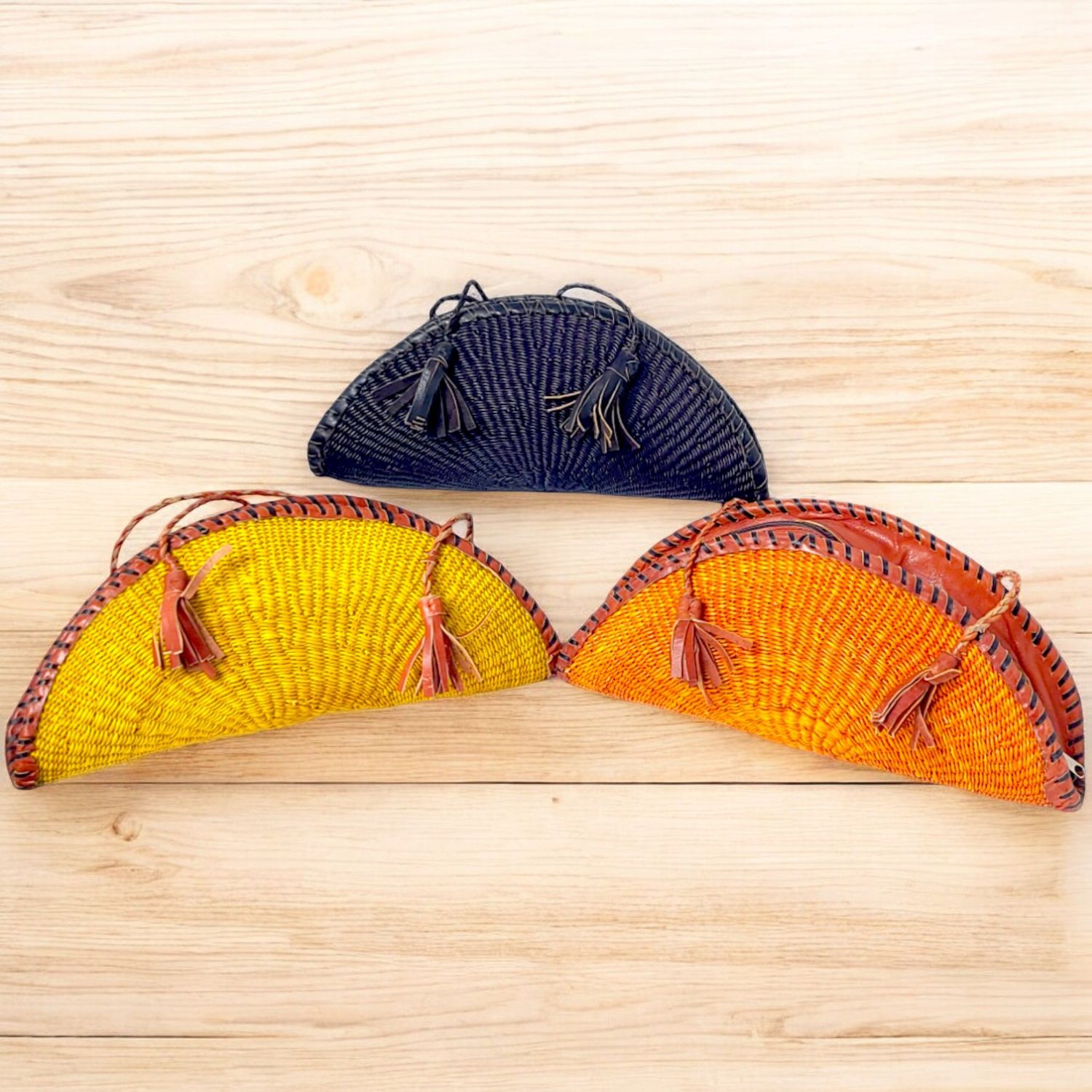 Three semicircular woven wicker bags with tassels. The bags are vibrant in yellow, orange, and black, creating a colorful and stylish display.