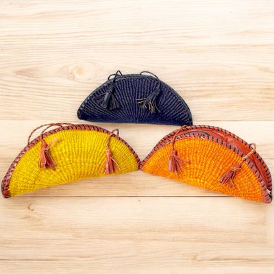 Three semicircular woven wicker bags with tassels. The bags are vibrant in yellow, orange, and black, creating a colorful and stylish display.