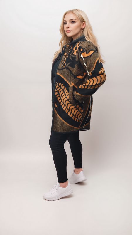 Blonde woman in a stylish black and orange patterned coat, black leggings, and white sneakers. She stands confidently against a light background.