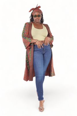 Woman in a colorful headwrap and robe, green crop top, and jeans. She wears sunglasses and heels, exuding confidence against a plain background.