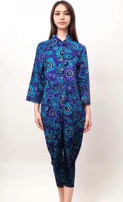 A woman wearing a vibrant, blue and purple paisley jumpsuit with long sleeves stands against a plain white background, conveying a chic and confident style.